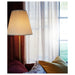 IKEA ÅRSTID brass floor lamp next to window diffusing warm light with red and mustard cushions nearby