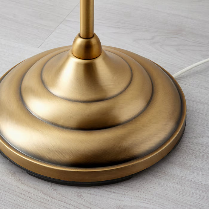 Close-up of IKEA ÅRSTID brass-finish floor lamp base with intricate curved metal stem detail