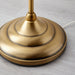 Close-up of IKEA ÅRSTID brass-finish floor lamp base with intricate curved metal stem detail
