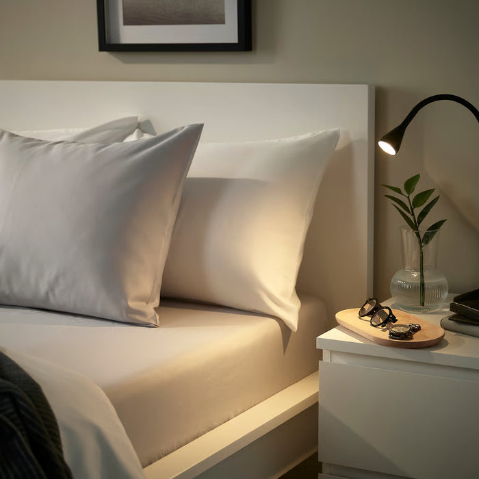 Bed dressed in soft grey IKEA BÄRGLIM fitted sheet beside white table with lamp and plant