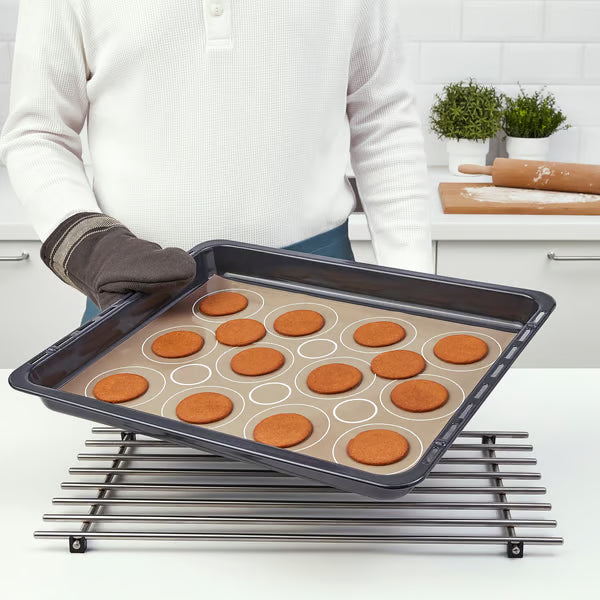 Person lifting baking tray with evenly baked cookies on IKEA BAKTRADITION mat over a cooling rack