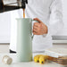 Person filling IKEA BEHÖVD light green vacuum flask on table with bananas and biscuits