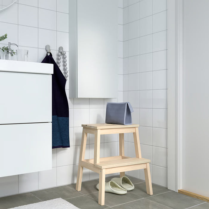 IKEA BEKVÄM wooden step stool in white bathroom beside sink with blue towel draped over top step