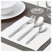 Silver cutlery set on a white napkin with a glass and plates in the background.