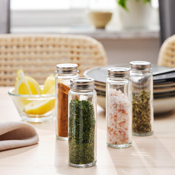 Person using IKEA CITRONHAJ spice jar to season stir-fried vegetables in copper skillet