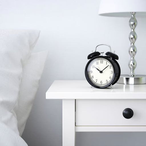 IKEA DEKAD black alarm clock on white bedside table beside lamp and pillow bedroom setting