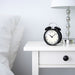 IKEA DEKAD black alarm clock on white bedside table beside lamp and pillow bedroom setting