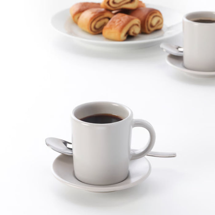 Two IKEA DINERA beige espresso cups on saucers with spoons and pastries lifestyle setting