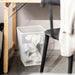 White mesh waste paper basket positioned under a wooden desk with visible leg protectors