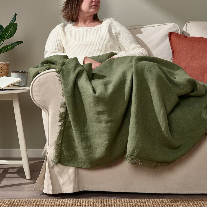 "Woman comfortably seated on a couch, enjoying the soft IKEA DYTÅG grey-green throw blanket"