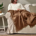 "Woman comfortably seated on a couch, enjoying the soft IKEA DYTÅG light brown throw blanket"