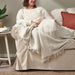 "Woman comfortably seated on a couch, enjoying the soft IKEA DYTÅG off-white throw blanket"