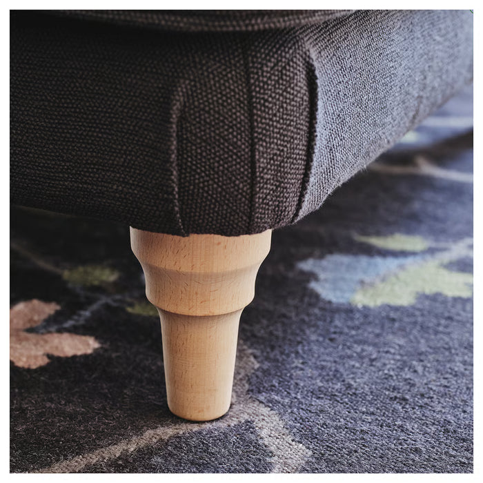 Close-up of a wooden leg of a piece of furniture on a patterned carpet