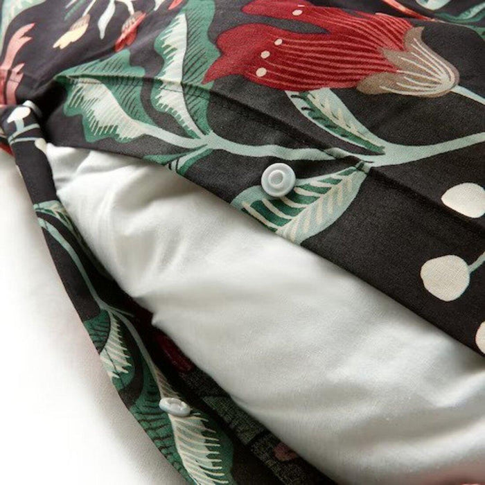 Close-up of a pillow inside a floral-patterned pillowcase with red, green, and white colors on a black background, secured with white buttons.50511635