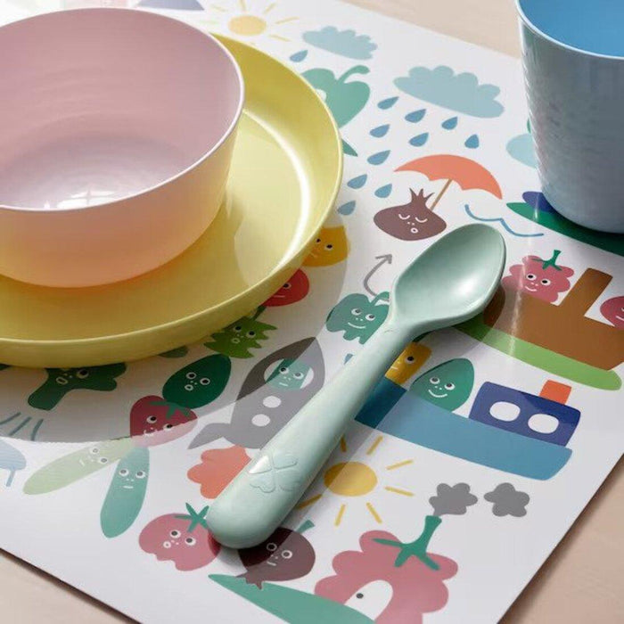 Children's tableware set with colorful bowl, plate, spoon, and cup on a patterned placemat.