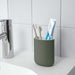 Bathroom countertop with a green toothbrush holder containing two toothbrushes and a tube of toothpaste. The countertop is white with a chrome faucet to the left. The background is white tiled walls-60496795, 00496798, 30496792