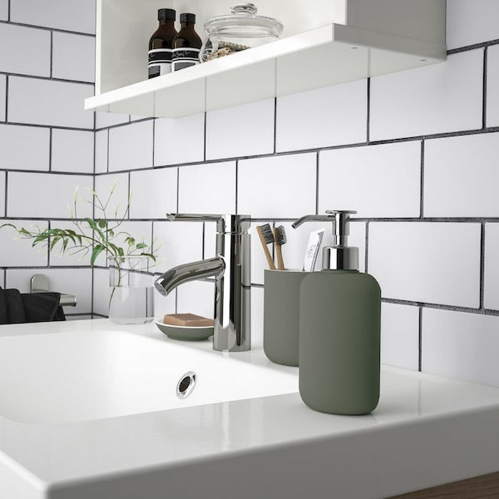 Modern bathroom sink area with a white sink and chrome faucet. On the right side of the sink, there is a green soap dispenser and a matching green container holding two toothbrushes and a tube of toothpaste. Above the sink, a white shelf displays two brown bottles and a glass jar with small items-60496795, 00496798, 30496792