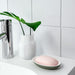 A bathroom sink area with a chrome faucet, a white ceramic vase containing green leaves, and a soap dish holding a pink bar of soap. The background consists of white tiled walls-60496795, 00496798, 30496792