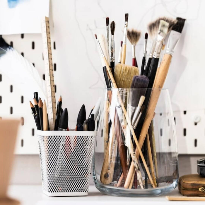 Collection of makeup brushes in glass containers on a white surface.