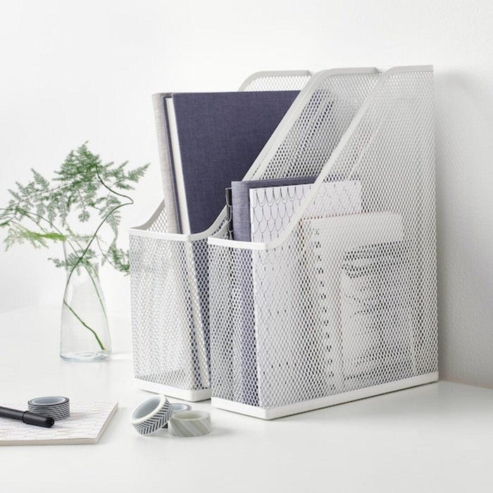 White mesh magazine holder with books on a white surface, with a plant in the background.