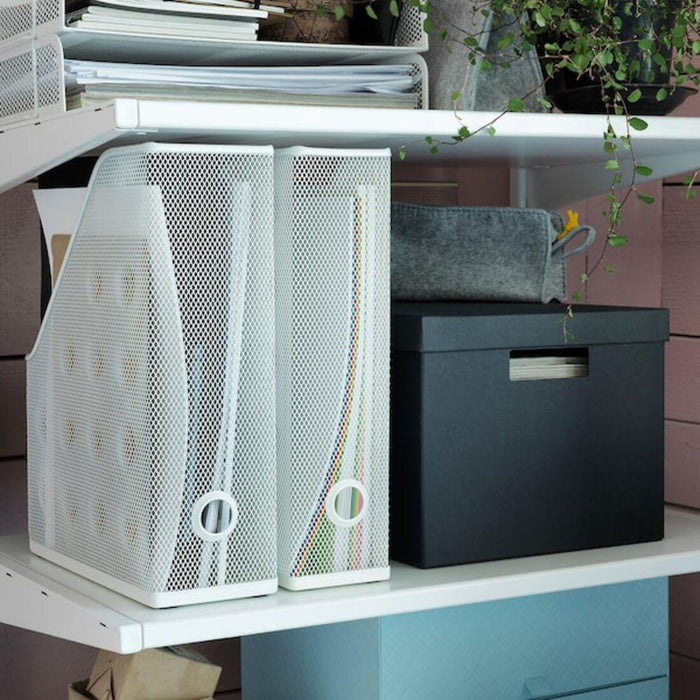 White mesh magazine holder with books on a desk next to a black storage box.