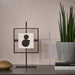 Modern black framed artwork on a stand next to a potted plant on a table.