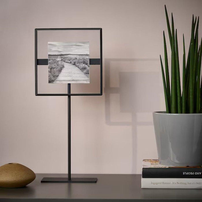 Framed artwork on a stand next to a potted plant on a table.