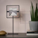 Framed artwork on a stand next to a potted plant on a table.