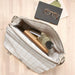 Open bag with grid pattern containing a water bottle, notebook, and glasses on a wooden surface