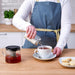 The shaker stands on a table next to a cup of coffee, ready to add sugar to the beverage.