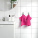 The cloth is neatly folded and placed on a wooden bathroom shelf, and its stylish color adds a pop of brightness to the scene.
