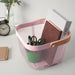Pink IKEA RISATORP basket, 25x26x18 cm (9 ¾x10 ¼x7 "), placed on a desk with office essentials. Features ventilated steel mesh with a sturdy wooden handle for easy portability. The basket contains books, a green cup with pens, pencils, and scissors, creating a well-organized workspace.-60588691
