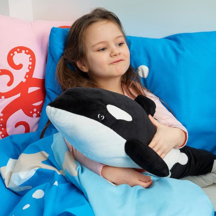 The IKEA Soft Toy Orca/Black White sitting on a couch with a child, providing a comfortable and huggable companion.