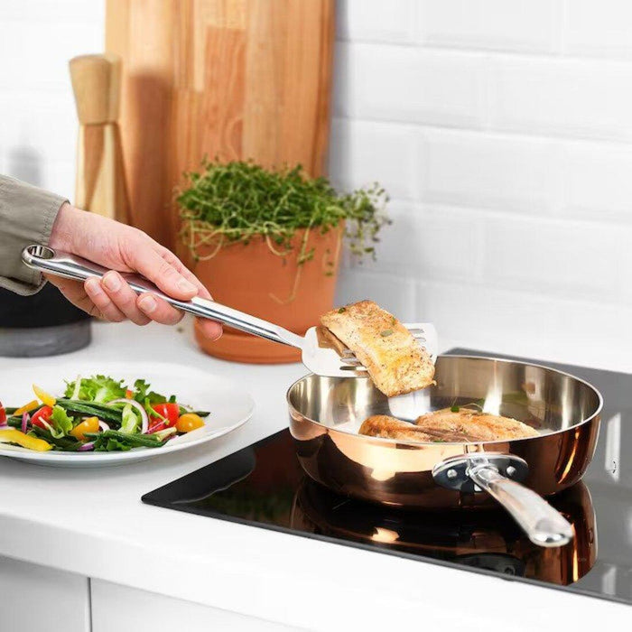 Person serving food from a stainless steel pan on a stove with a plate of salad in the foreground.