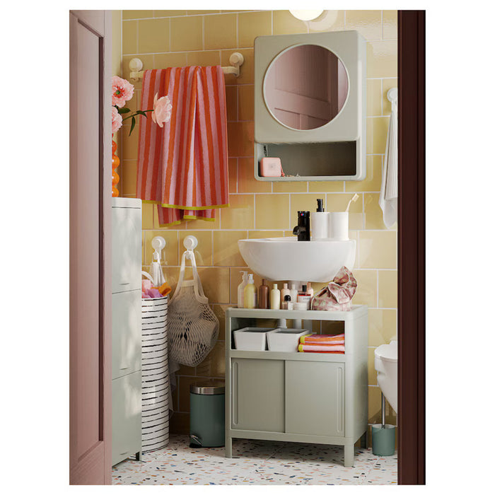 The image depicts the IKEA IVÖSJÖN wash-basin base cabinet in green, measuring 50x33x57 cm (19 5/8x13x22 1/2 inches). Positioned beneath a white washbasin, it features sliding doors that provide convenient storage for toiletries. The cabinet is styled in a modern, organized bathroom setting with complementary elements like a wall-mounted mirror cabinet, colorful striped towel, hanging mesh bags, and a terrazzo-patterned floor-00597293   