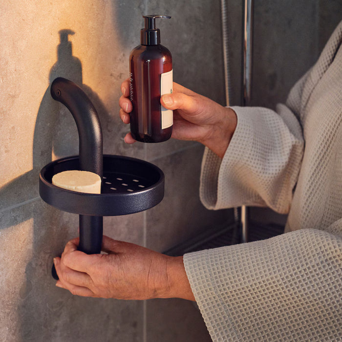 A person wearing a light-colored textured bathrobe holds a brown bottle with a pump dispenser, likely containing liquid soap or lotion.-90595992