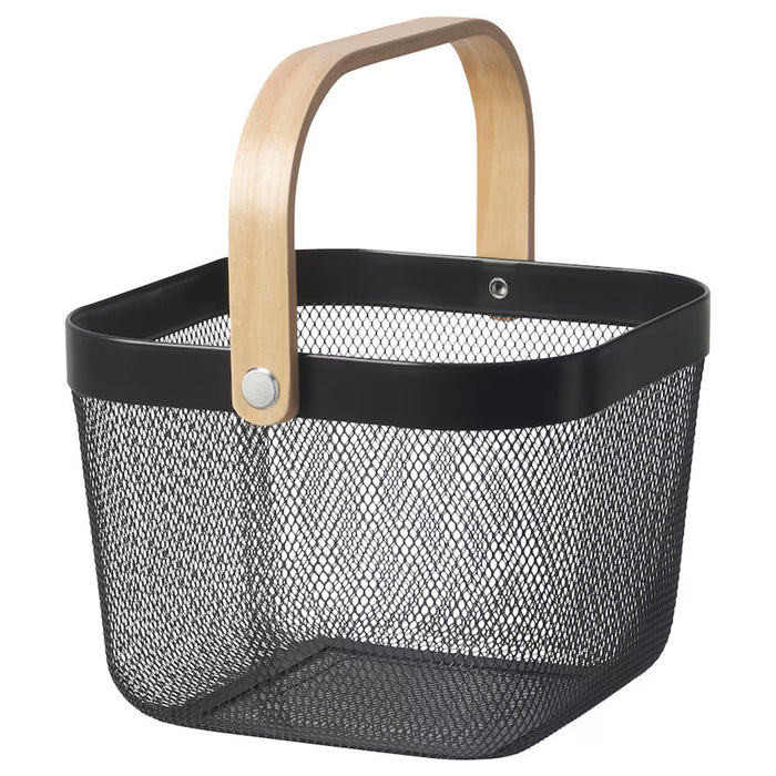 Dark grey IKEA RISATORP basket, 25x26x18 cm (9 ¾x10 ¼x7 "), placed on a white table beside a ceramic mug. Ventilated steel mesh with a sturdy wooden handle for easy portability.-00588712