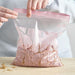 A person placing a cinnamon roll into an IKEA ISTAD resealable bag with a pale pink geometric pattern. The bag features a double-seal strip for secure closure.-80592710