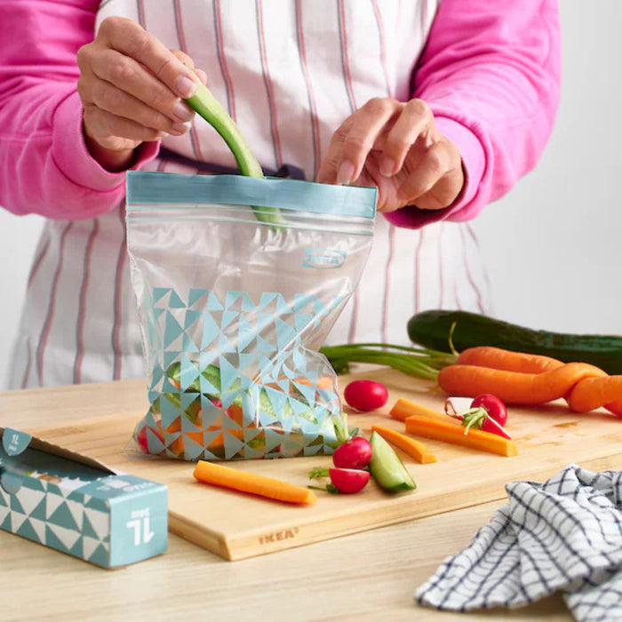 A person placing an IKEA ISTAD resealable bag filled with food into a freezer drawer. The freezer contains other stored items, demonstrating the bag’s suitability for freezing and preserving contents.-50592716
