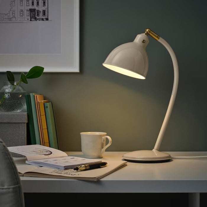 A stylish IKEA RÖDFLIK desk lamp in light beige with a vintage industrial design, featuring a shiny enamel-like finish, brass-colored accents, and an adjustable shade with a toggle switch for precise lighting control-20583921   
