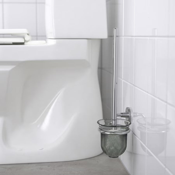 The wall-mounted chrome toilet brush holder is in a sleek bathroom setting, featuring white tiled walls, a modern toilet, and light-colored flooring for a clean aesthetic.- 90581551