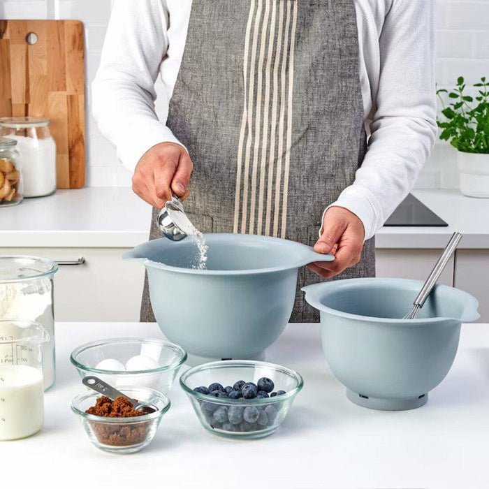 Person preparing ingredients in a kitchen with blue mixing bowls and small glass bowls.