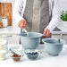 Person preparing ingredients in a kitchen with blue mixing bowls and small glass bowls.