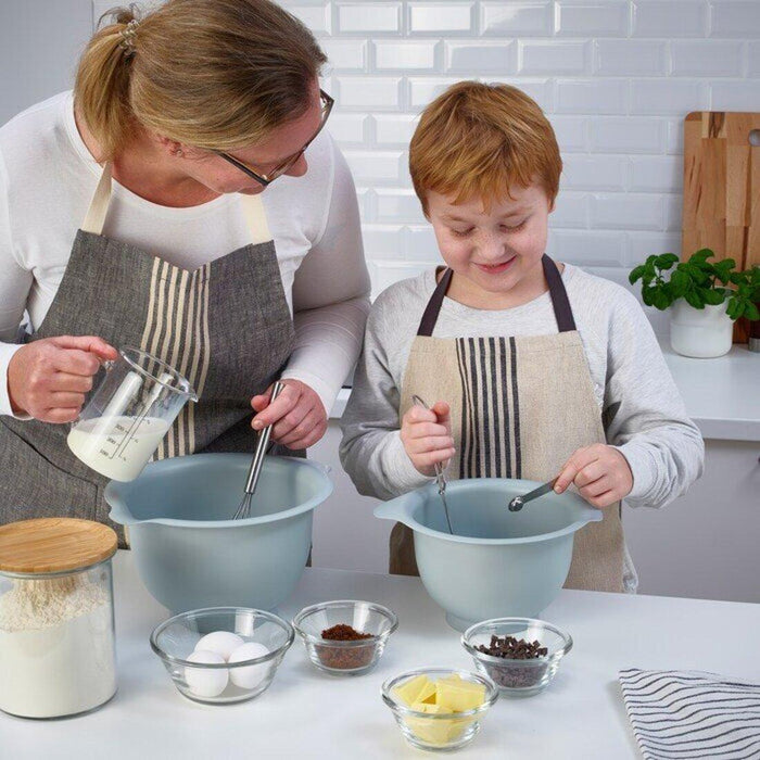 Woman and child in aprons mixing ingredients in bowls in a kitchen.