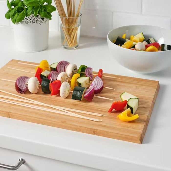 Colorful vegetable skewers on a wooden cutting board with a bowl of salad in the background.