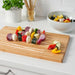 Colorful vegetable skewers on a wooden cutting board with a bowl of salad in the background.
