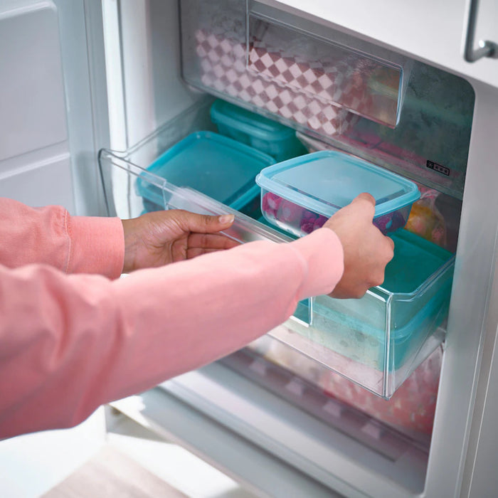 A person placing an IKEA PRUTA food container with a blue lid, 0.6 l (20 oz), into a transparent freezer drawer. The container is part of an organized set of similar containers, demonstrating efficient food storage-60597105 