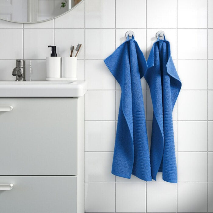 The cloth is neatly folded and placed on a wooden bathroom shelf, and its stylish color adds a pop of brightness to the scene.