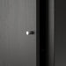 A close-up view of a black-brown IKEA KALLAX insert with a door, highlighting its smooth surface texture and small, round metallic knob centered on the door panel. The door is slightly ajar, revealing a dark interior, emphasizing the hidden storage functionality. The minimalist design complements modern home organization while providing a stylish solution for discreet storage.