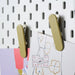 Close up image of Beige-green IKEA pegboard clip holding various items on a pegboard